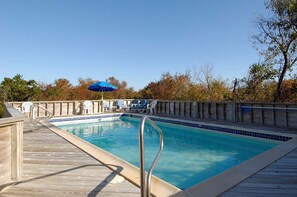 Ein Schwimmbecken mit Holzterrasse, Liegestühlen und einem blauen Sonnenschirm.