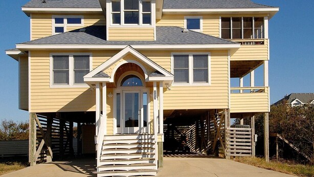 A two-story house with a front porch, a garage, and a balcony. - 2060 - DoodleBug - Corolla Retreat | Private Pool & Walk to Beach (Corolla)