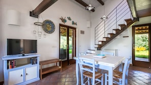 A dining area with a table and chairs, a television on a cabinet, and a staircase leading to another level.