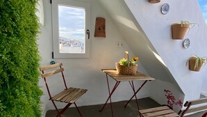 A cozy corner with a wooden table and two chairs, surrounded by potted plants and a view of the city.