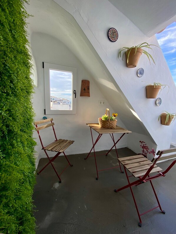 A cozy corner with a wooden table and two chairs, surrounded by potted plants and a view of the city.