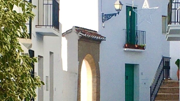 A white building with a green door, a small balcony, and a staircase leading to the entrance.