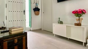 A room with a white door, a green-framed window, a white console table with a vase of flowers, and a mounted TV.