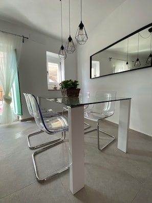 A modern dining area with a glass table and metal chairs, a hanging light fixture, and a large mirror on the wall.