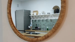 A kitchen with a round mirror, a refrigerator, a sink, and a shelf with kitchenware.