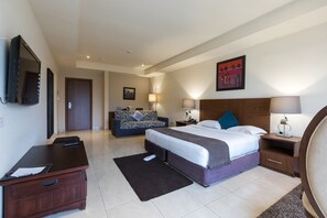 A hotel room with a large bed, a desk, a chair, a TV, and a painting on the wall.