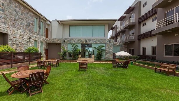 A courtyard with outdoor seating, stone walls, and a modern building with large windows. - Lodge by Eagles (Sekondi-Takoradi)