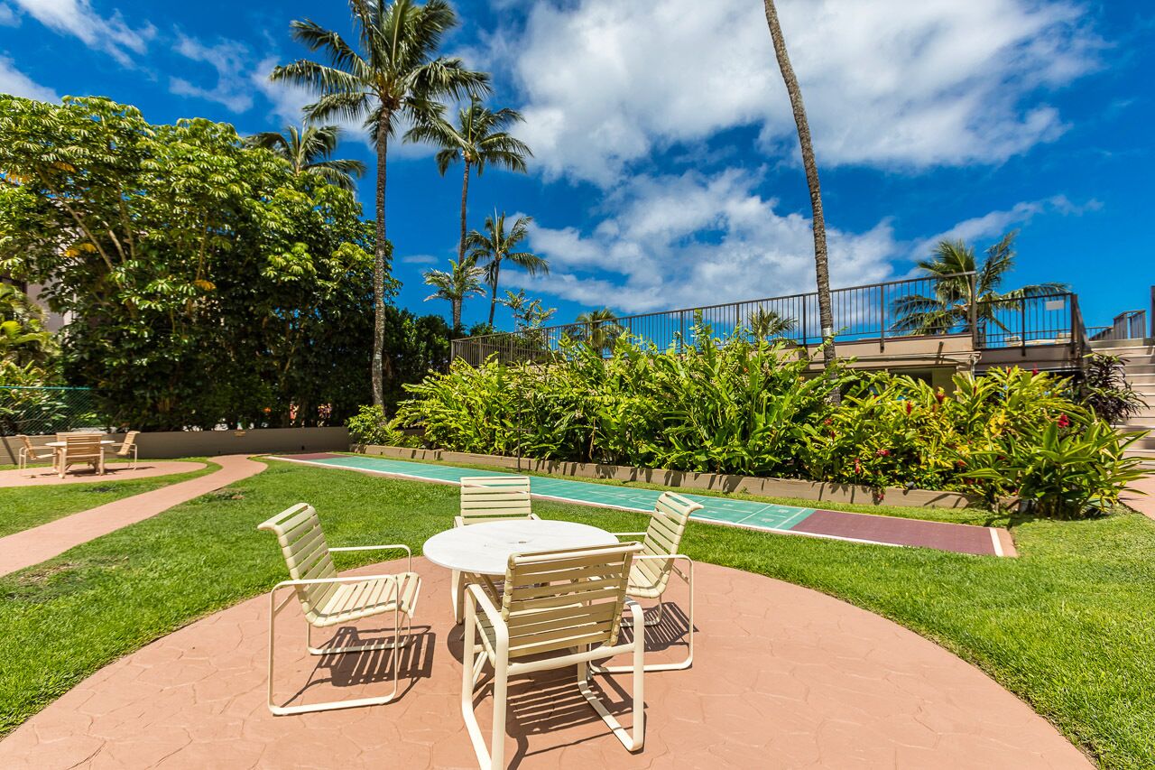 Un espace aménagé au bord de la piscine, avec une table ronde et des chaises, entouré d’une végétation luxuriante et de palmiers.