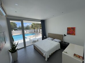A modern hotel room with a large bed, a bedside table, a desk, and a view of an outdoor swimming pool.