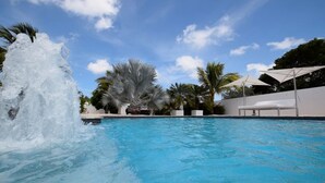 A swimming pool with a water fountain, surrounded by palm trees and white umbrellas. - Luxury 4 bed Villa - Private Pool - Sleeps 8 (Jan Thiel)