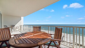 Een houten tafel en stoelen op een balkon met uitzicht op een strand en een heldere lucht.