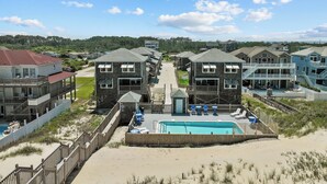 Un complexe hôtelier situé en bord de mer, composé de plusieurs bâtiments à deux étages, d’un espace piscine central et d’une plage de sable.