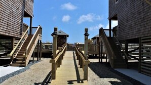 Une promenade en bois mène à une zone de plage bordée de bâtiments des deux côtés.