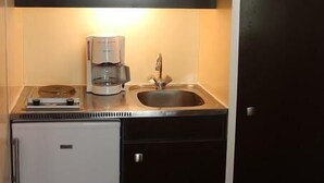 Una cucina compatta con macchina del caffè, lavello e piccolo frigorifero.