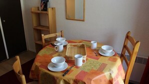 Zona pranzo con tavolo apparecchiato per quattro persone, circondato da sedie di legno. Si vedono a sfondo una libreria e uno specchio.