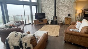 Un salón amplio con sofás de cuero, un televisor de pantalla plana grande, una pared de piedra y una chimenea.