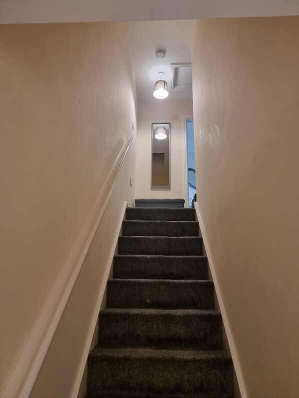 A carpeted staircase with a handrail, leading to a door with a light fixture above it. - Impeccable Beachfront 2-bed Cottage in St Bees (St Bees)