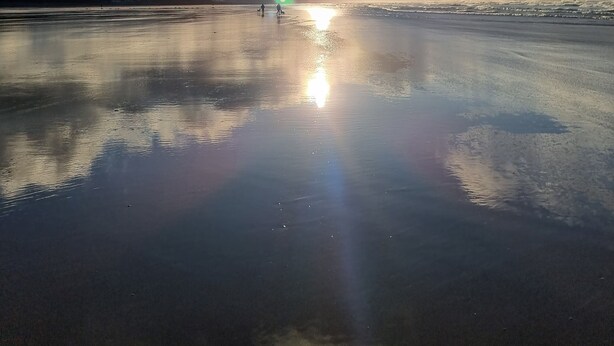 Una playa con mar tranquilo, cielo despejado y reflejos de sol sobre la arena mojada.