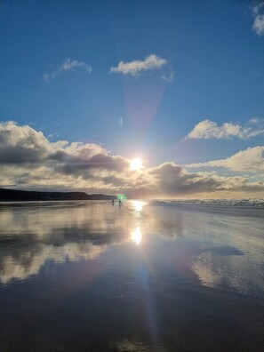 A beach with a calm sea, clear sky, and sunlight reflecting on the wet sand. - Impeccable Beachfront 2-bed Cottage in St Bees (St Bees)