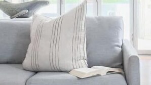 A grey sofa with striped pillows and a book, positioned in a room with large windows. - On Northpoint at Salt (Kingscliff)