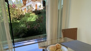 A breakfast table with a plate of food, a glass of orange juice, a cup of coffee, and a view of a building through a window. - Pousada Vale do Chapéu (Capitólio)
