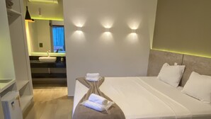 A bedroom with a bed, bedside tables, and a nightstand. There is a window with curtains, a wall-mounted air conditioner, and a light fixture above the bed. - Pousada Vale do Chapéu (Capitólio)