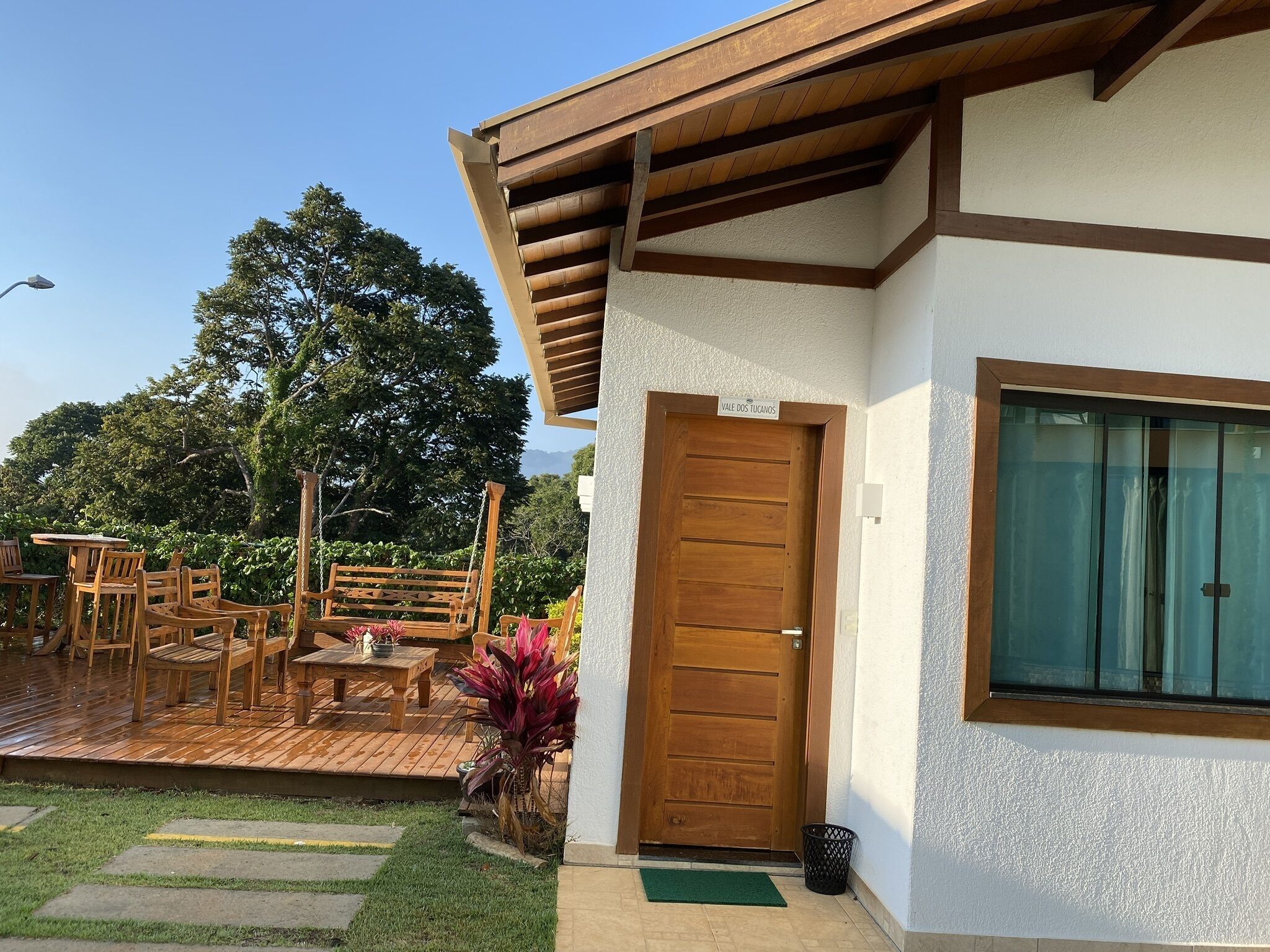 A wooden deck with outdoor furniture, a wooden door, and a window with curtains.