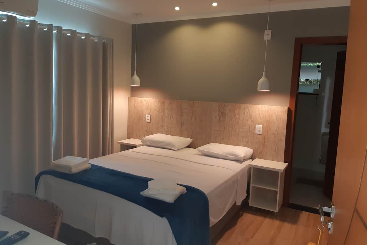 A modern hotel room with a large bed, bedside tables, and a wooden headboard.