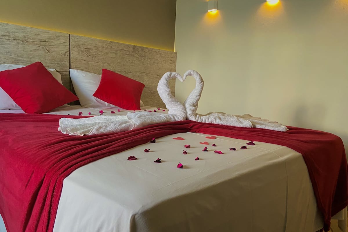 A hotel room with a neatly made bed, red and white bedding, and a heart-shaped towel arrangement on the bed.