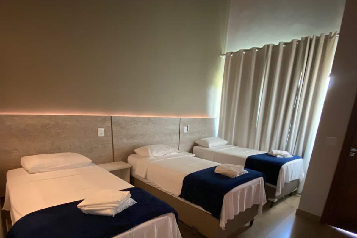 A hotel room with three single beds, each with a white and blue bedspread, and a wooden floor.