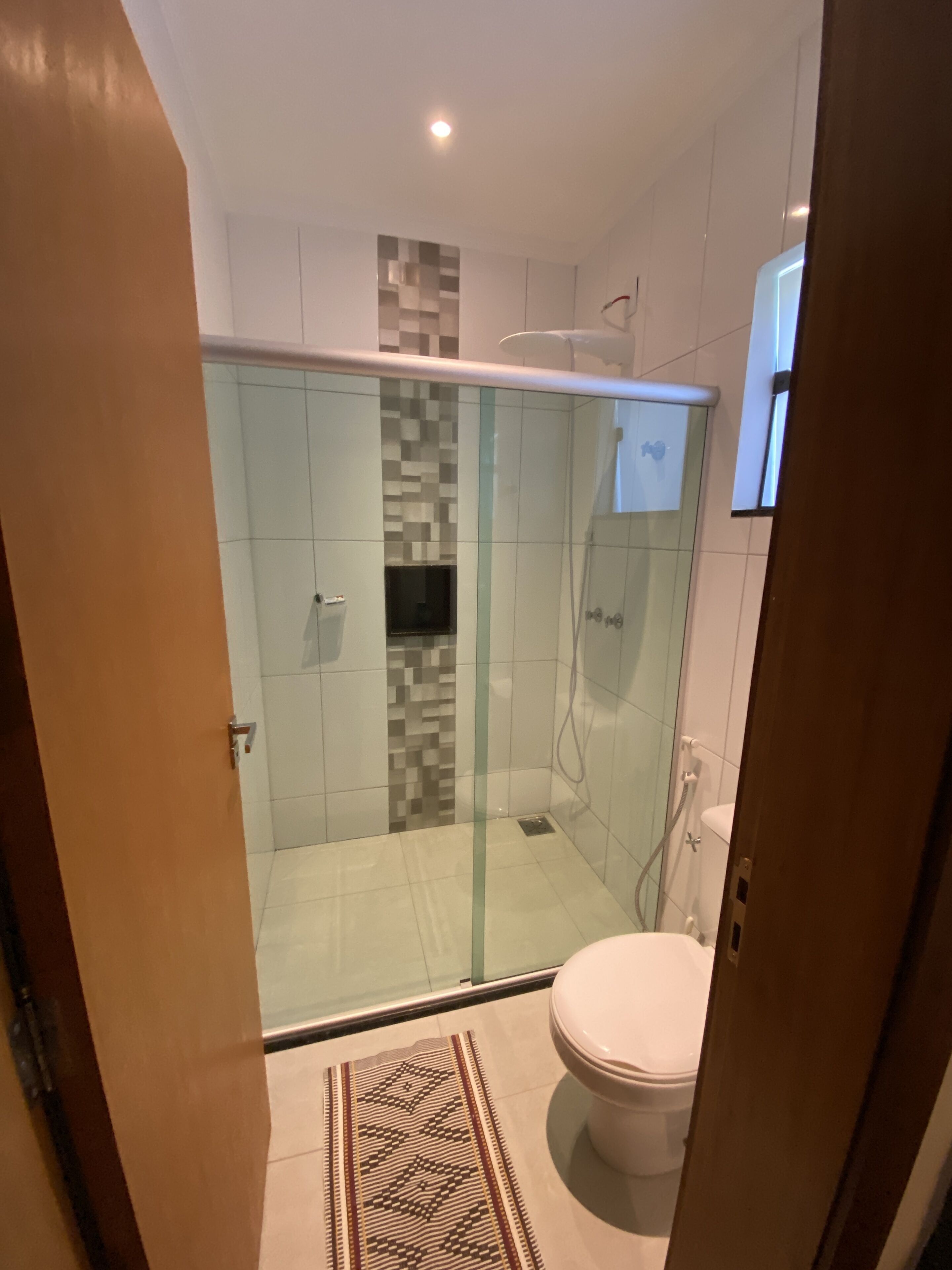 A modern bathroom with a glass-enclosed shower, a toilet, and a patterned rug.