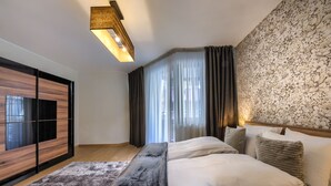 Een moderne slaapkamer met een groot bed, een flatscreen televisie, een houten garderobe en een behang met een patroon.