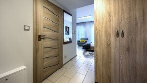 Een hal met houten deuren, een radiator, en een blik op een zithoek met een bank en gordijnen.