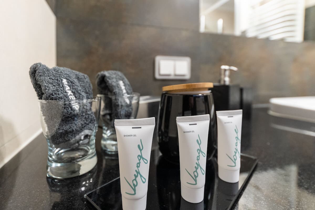 A bathroom counter with two shower gel tubes labeled "Voyage," a glass with a towel, and a black soap dispenser.