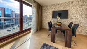Een moderne hotelkamer met een groot raam, een flatscreen televisie aan de wand, een houten eettafel met stoelen en een bloemenmotief op de muur.