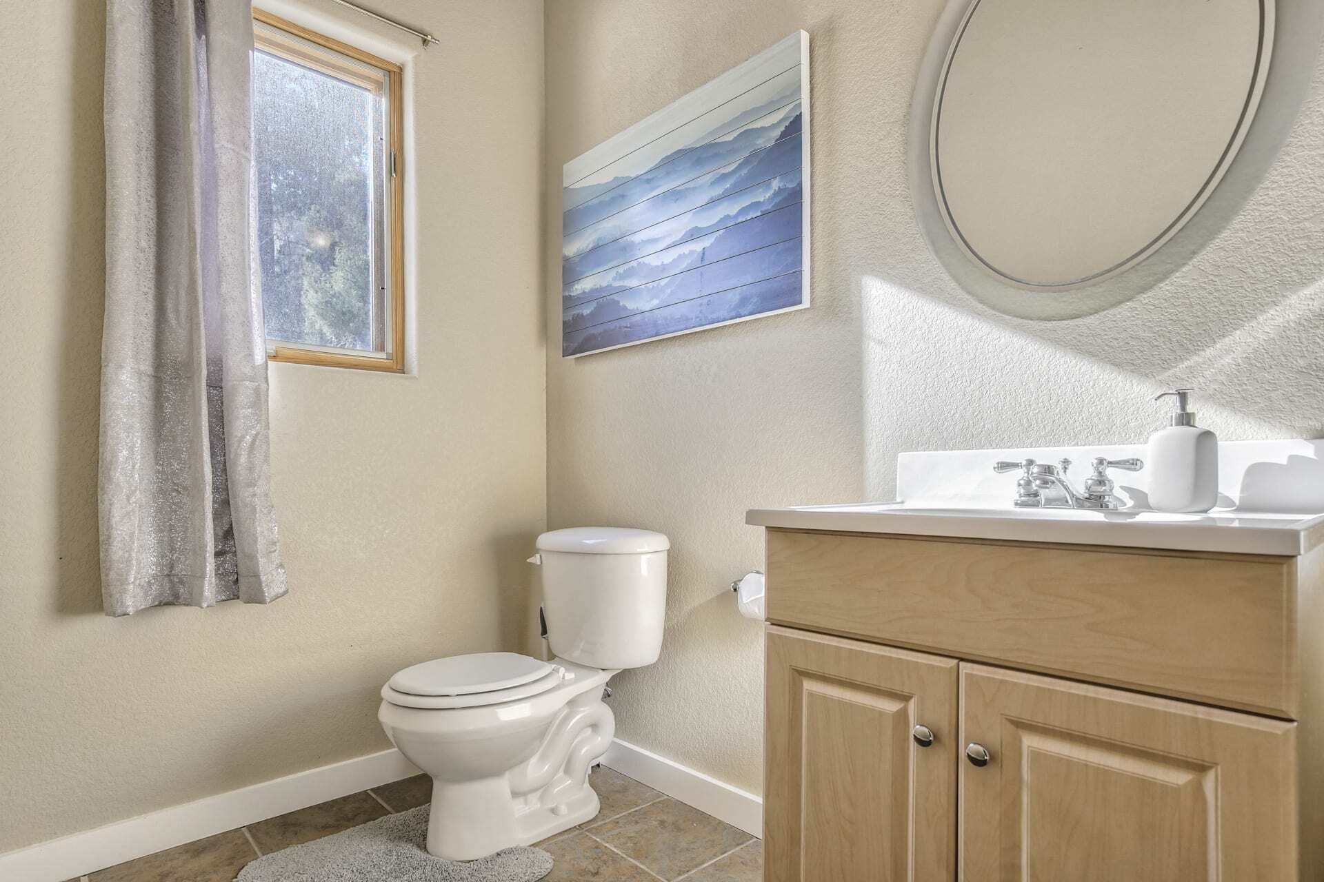 A bathroom with a toilet, a sink with a mirror, and a painting on the wall.