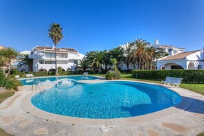 A swimming pool surrounded by palm trees and a white building with a tiled roof.