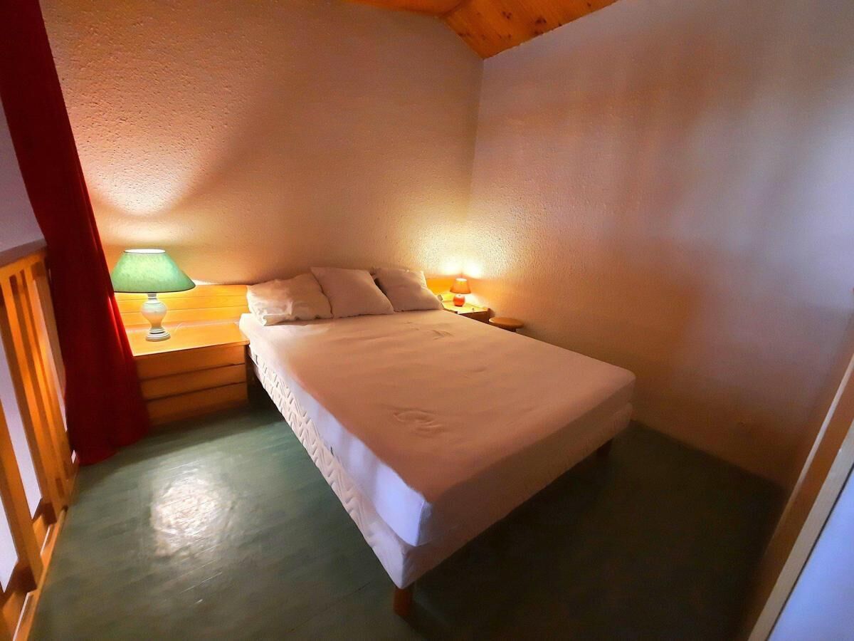 A small, cozy bedroom with a single bed, a nightstand with a lamp, and a wooden headboard.