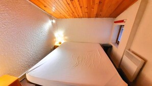 Ein kleiner, gemütlicher Raum mit einem Einzelbett, einer Holzbalkendecke und einem kleinen Fenster.