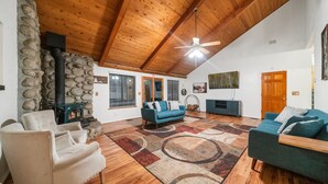 A spacious living room with a stone fireplace, wooden ceiling, and a large ceiling fan. - Family Retreat: Near Town, Hot Tub, AC, (Idyllwild)