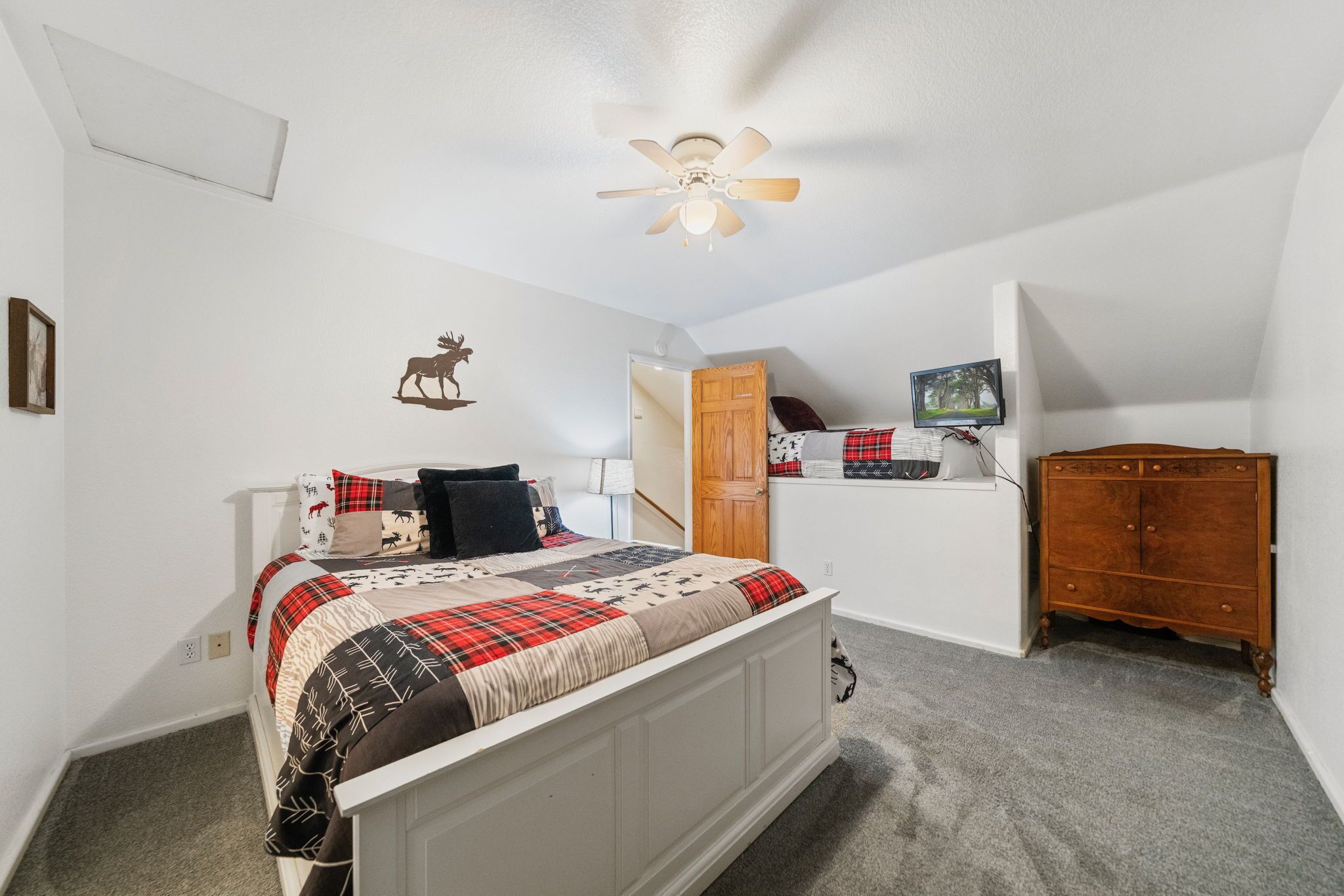 A bedroom with a bed, a ceiling fan, a dresser, and a TV on a shelf.