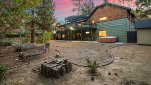 A two-story house with a covered patio, a wooden deck, and a landscaped backyard with a bench and a tree stump. - Family Retreat: Near Town, Hot Tub, AC, (Idyllwild)