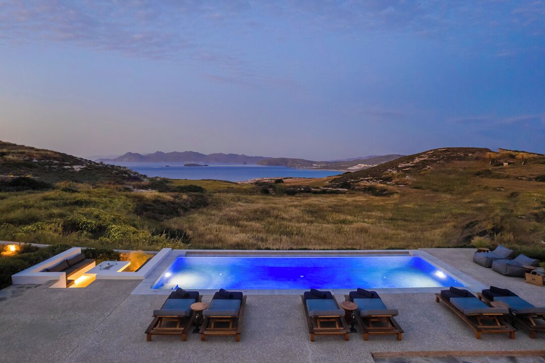 A pool area with lounge chairs and a view of the sea.