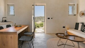 A modern kitchen with a wooden island, black woven chairs, and a view of the desert through an open door. - Ventus di Milo (Milos)