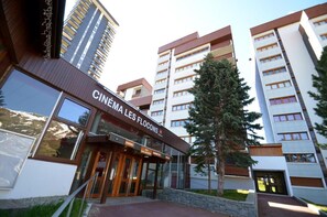 A cinema building with a modern facade, large windows, and a sign reading "CINEMA LES FLOCONS". - 50m from resort center, 13rd floor, view mountain, balcony, tv, 25m², Les Menuires (Les Menuires)