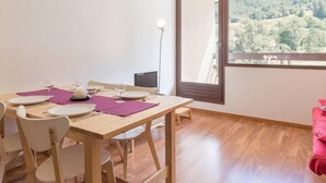 A dining area with a wooden table set for four, a large window with a view of a forested area, and a pink couch in the corner. - 4th floor, view ski slopes, balcony, parking, 28m², Serre Chevalier (SERRE CHEVALIER)