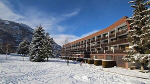 A hotel with multiple floors, a snow-covered landscape, and mountains in the background. - 4th floor, view ski slopes, balcony, parking, 28m², Serre Chevalier (SERRE CHEVALIER)