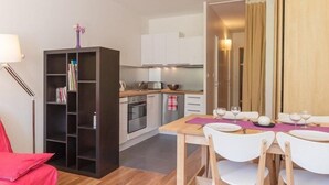 A compact kitchen with white cabinets, a dining area with a table set for two, and a bookshelf with books. - 4th floor, view ski slopes, balcony, parking, 28m², Serre Chevalier (SERRE CHEVALIER)