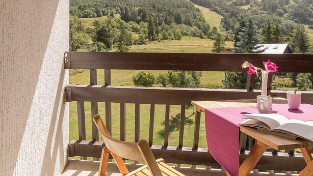 A balcony with a wooden railing, a table with a pink tablecloth, a chair, and a vase with pink flowers. - 4th floor, view ski slopes, balcony, parking, 28m², Serre Chevalier (SERRE CHEVALIER)