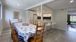 Een eetgedeelte met een tafel gedekt voor zes personen, houten stoelen, een rieten mand en een keuken op de achtergrond.